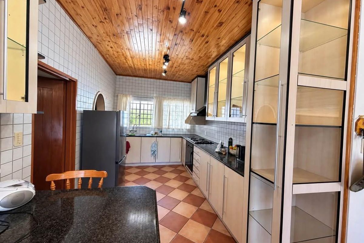 A functional kitchen featuring granite countertops, built-in cabinetry, glass display units, and a distinctive timber ceiling, offering a classic layout with ample storage space.