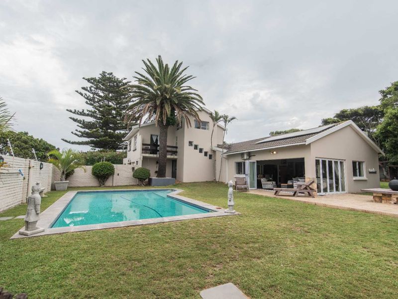 Rear view of the property featuring a swimming pool, landscaped garden, paved patio area, and multi-level building structure with balcony.