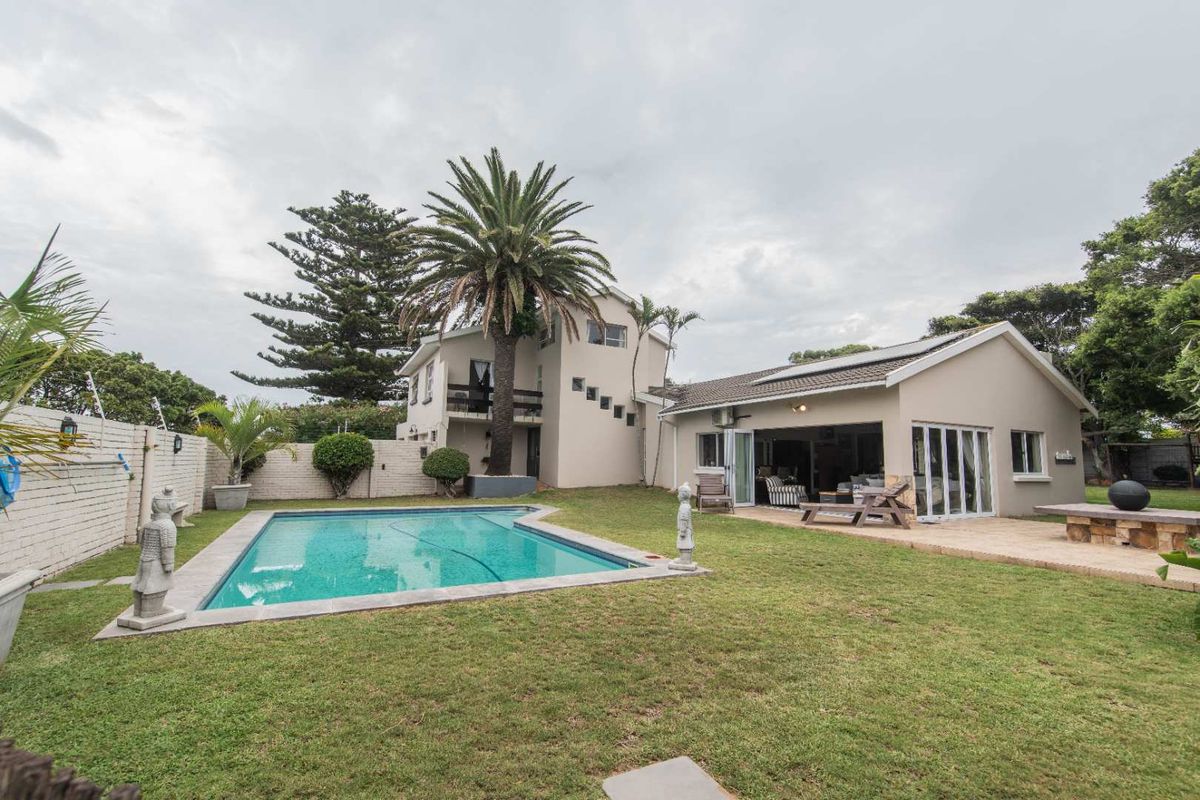 Rear view of the property featuring a swimming pool, landscaped garden, paved patio area, and multi-level building structure with balcony.