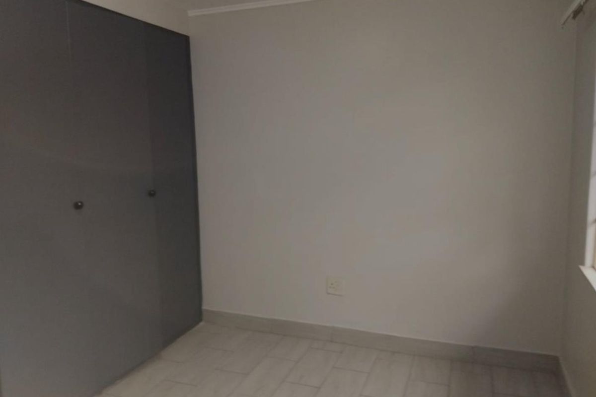 An empty bedroom featuring neutral tiled flooring and dark grey built-in cupboards, providing a clean and versatile space.
