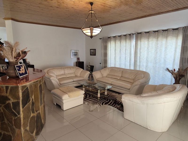 Spacious living room featuring a unique built-in stone bar, warm timber ceiling, and large windows with natural light, finished with neutral floor tiles.