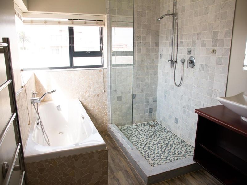 Modern bathroom featuring a walk-in shower with mosaic tiling, a separate built-in bathtub, marble wall finishes, and a heated towel rail.