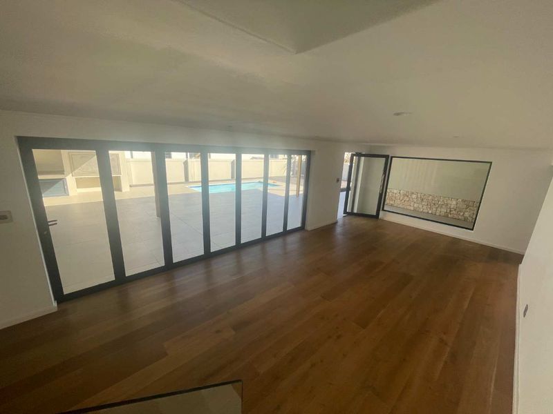 Spacious, light-filled living area featuring high-quality timber flooring, modern aluminium stacker doors opening to the pool area, and a contemporary stone feature wall.