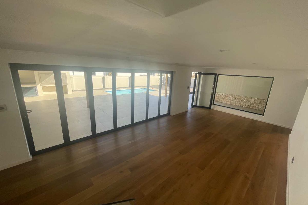 Spacious, light-filled living area featuring high-quality timber flooring, modern aluminium stacker doors opening to the pool area, and a contemporary stone feature wall.