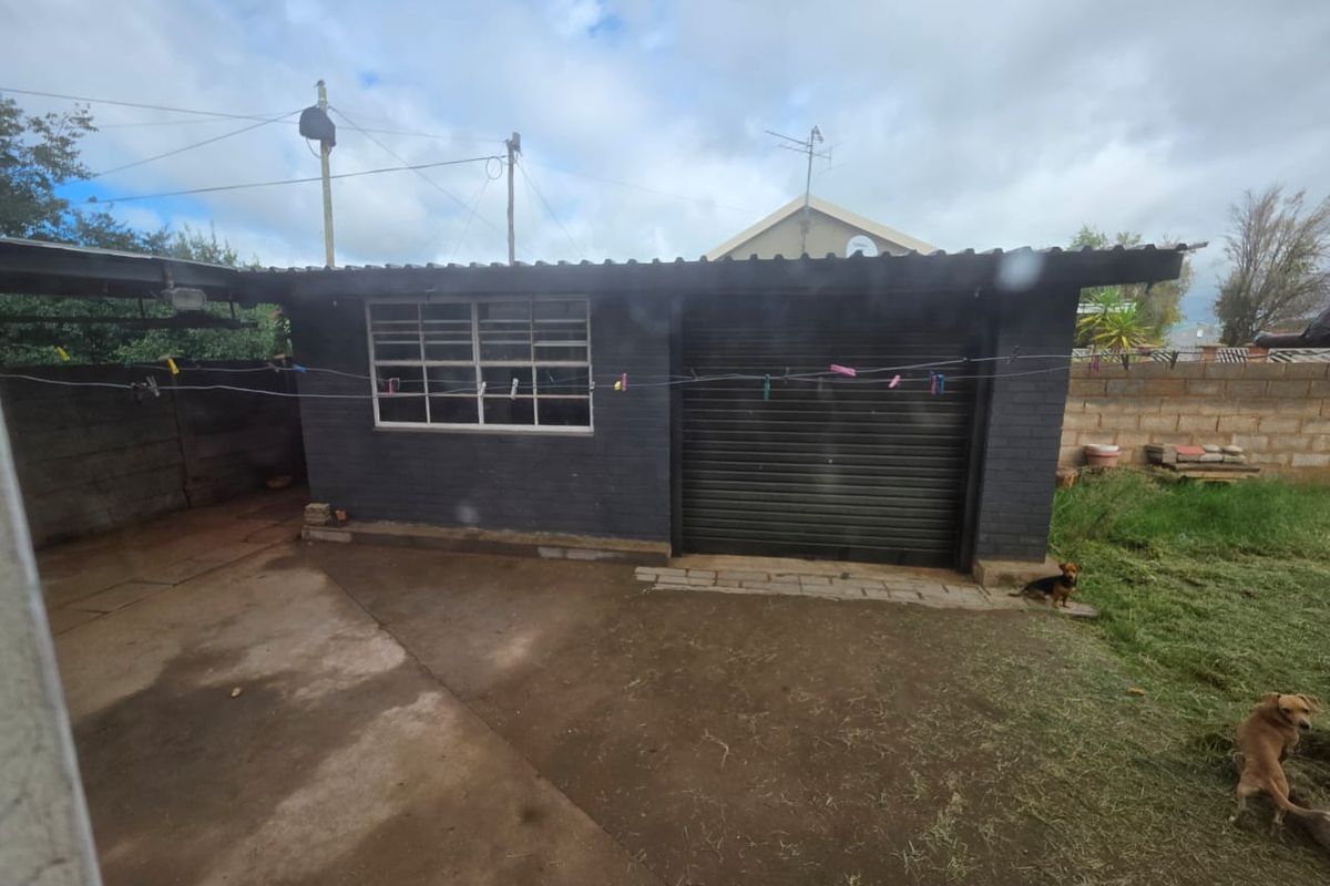 A detached garage structure featuring a roller shutter door and metal-framed window, set within a paved and grassed rear yard area.