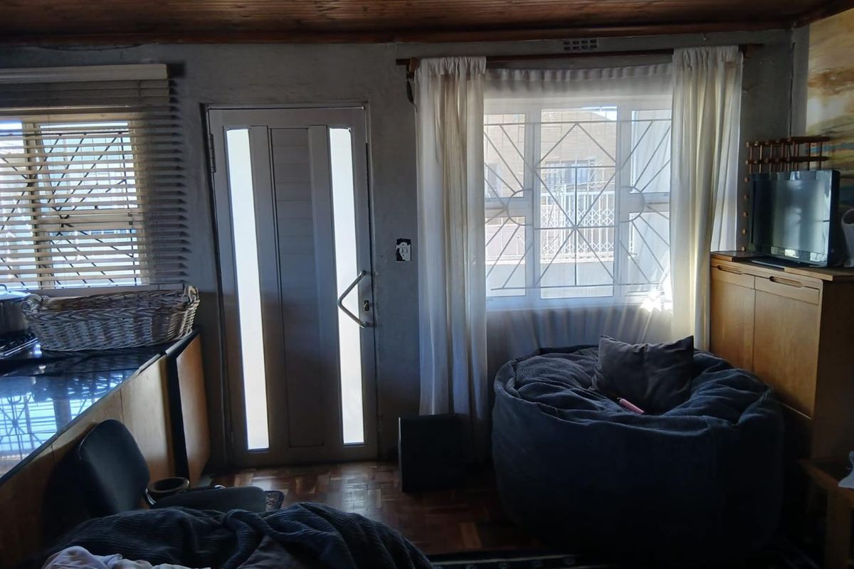 A living area featuring parquet flooring, a timber-paneled ceiling, and a security-gated entrance door with natural light from multiple windows.