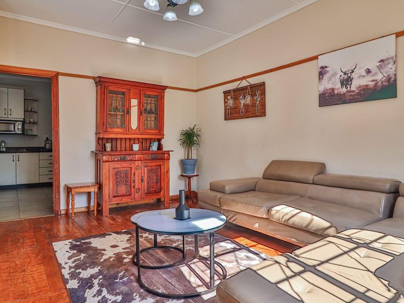 A comfortable living room featuring warm hardwood flooring and a classic picture rail, with an open doorway leading to the kitchen area.