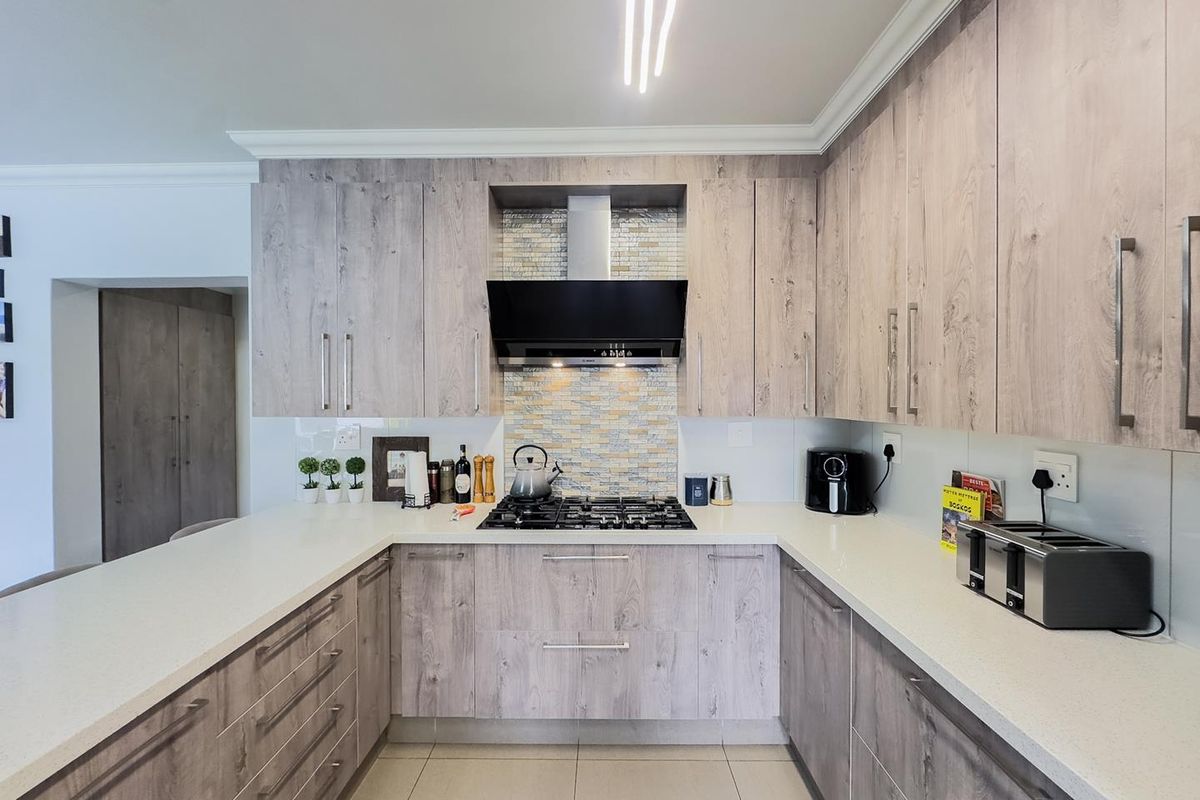 Modern U-shaped kitchen featuring light wood-grain cabinetry, stone countertops, a gas hob, and a mosaic tile backsplash.