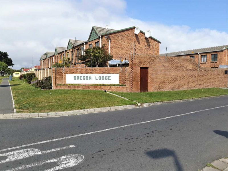 Street view of the Oregon Lodge townhouse complex, featuring face brick construction, tiled roofing, and perimeter security fencing.