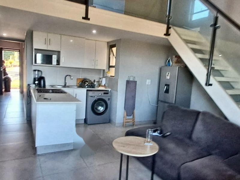 Open-plan living area featuring a modern kitchen with built-in cabinetry, tiled floors, and a staircase with a glass balustrade leading to an upper level.