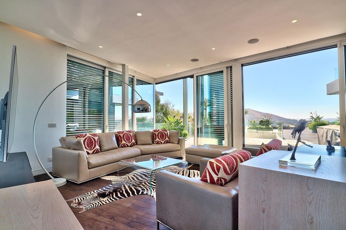 Modern living room featuring expansive floor-to-ceiling sliding glass doors, recessed lighting, integrated ceiling speakers, and high-quality hardwood flooring with seamless outdoor access.