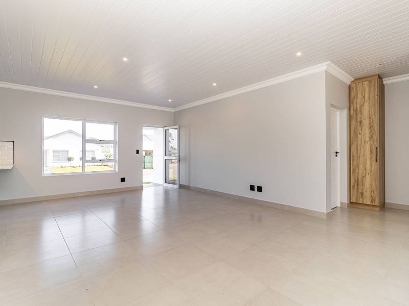 A bright, modern open-plan living and kitchen area featuring neutral tiled floors, a tongue and groove ceiling, and clean, contemporary finishes.