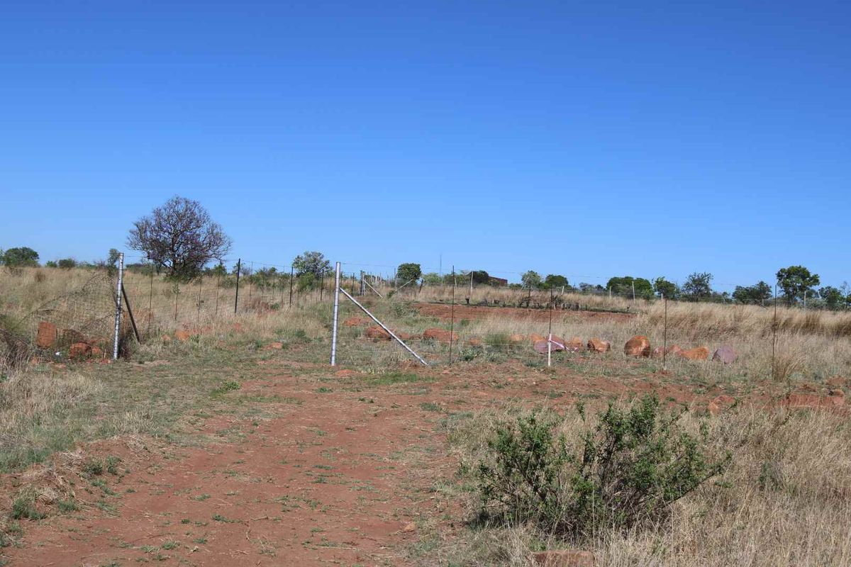 An expansive, undeveloped plot of land featuring natural dry grass, scattered rocks, and perimeter wire fencing under a clear blue sky.