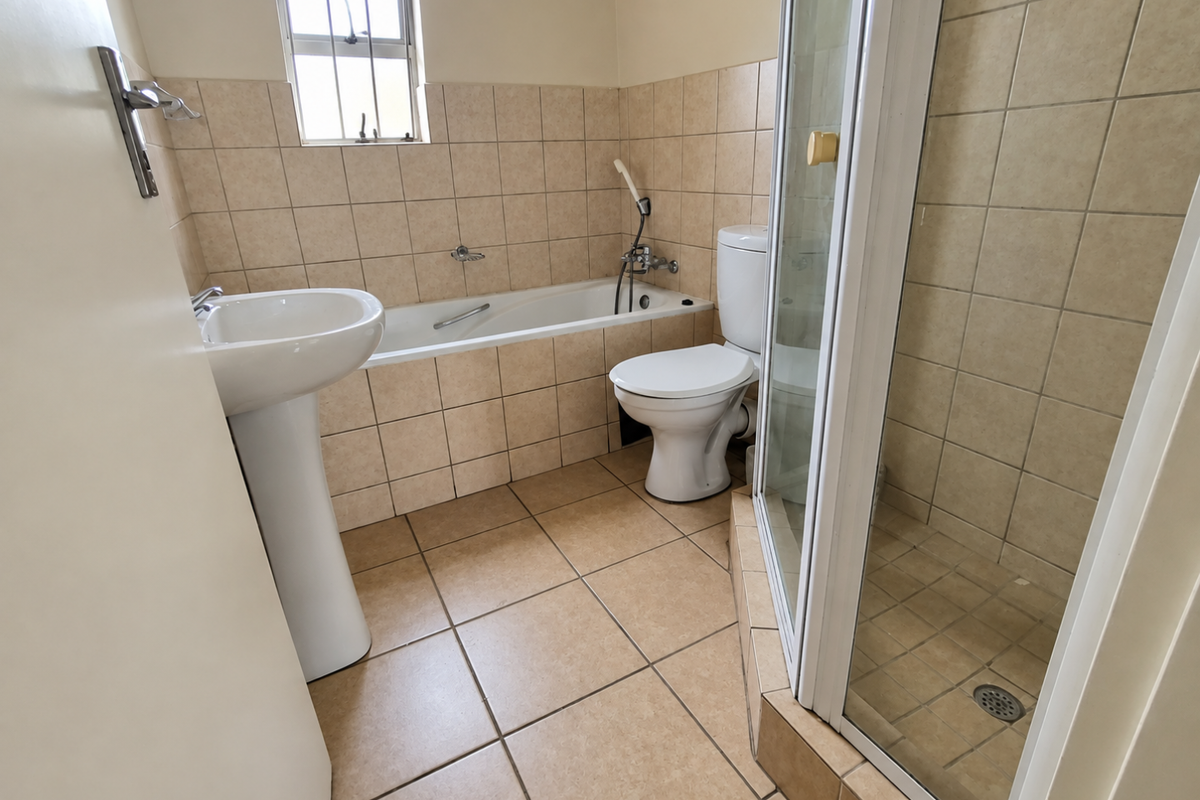 A functional bathroom featuring a pedestal basin, built-in bathtub, toilet, and a separate corner shower enclosure with neutral ceramic tiling throughout.