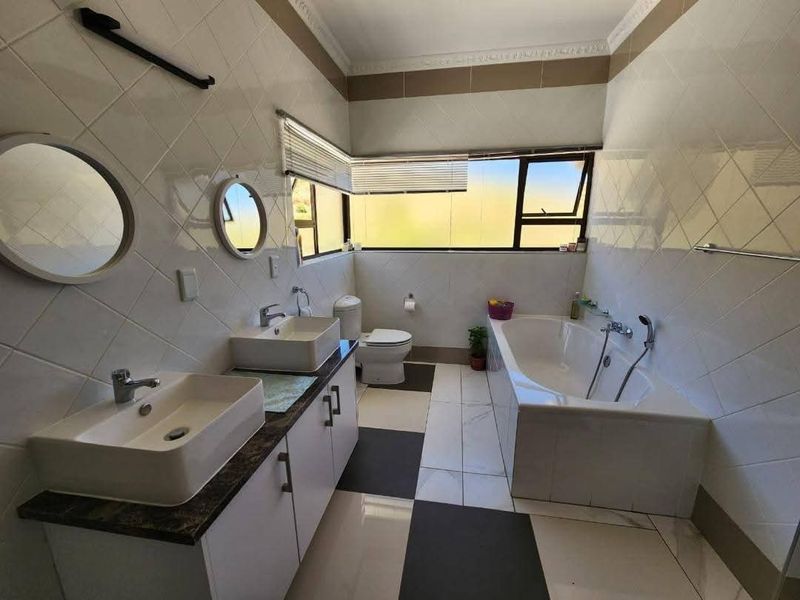 A well-lit bathroom featuring a double vanity with vessel sinks, a built-in bathtub, and modern tiled finishes throughout.