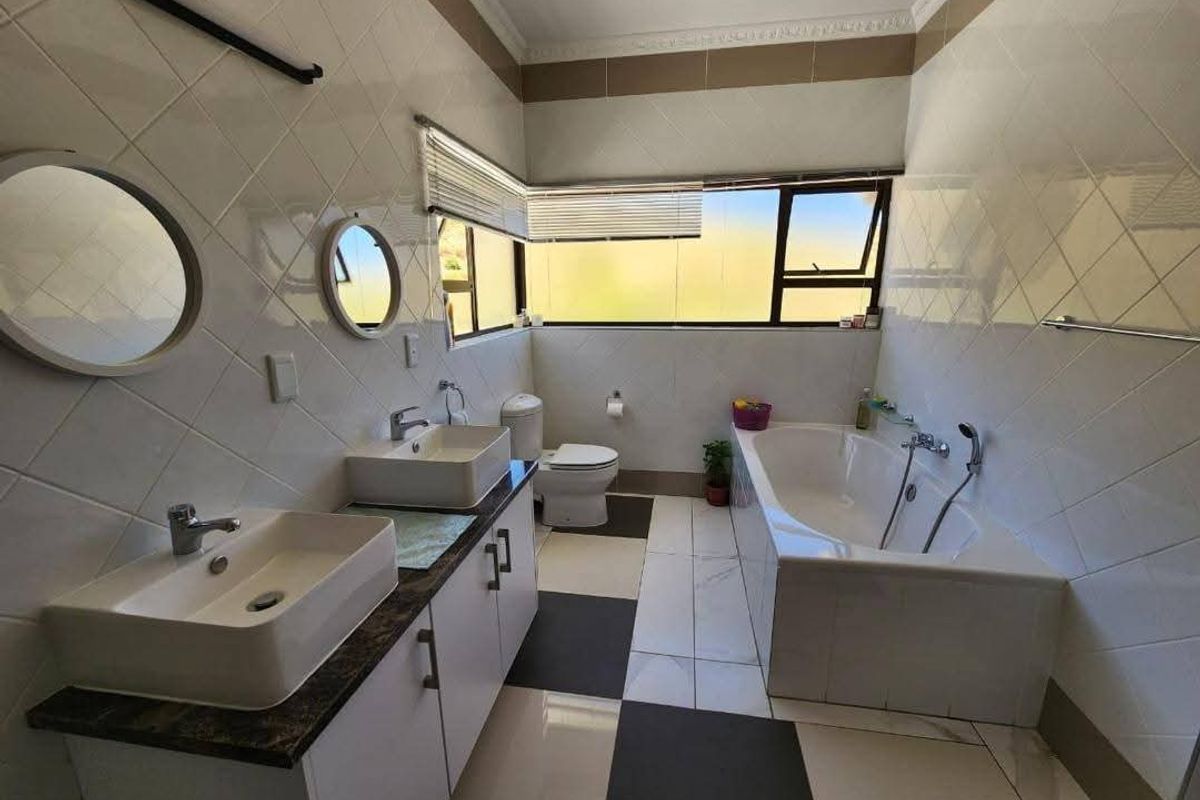 A well-lit bathroom featuring a double vanity with vessel sinks, a built-in bathtub, and modern tiled finishes throughout.