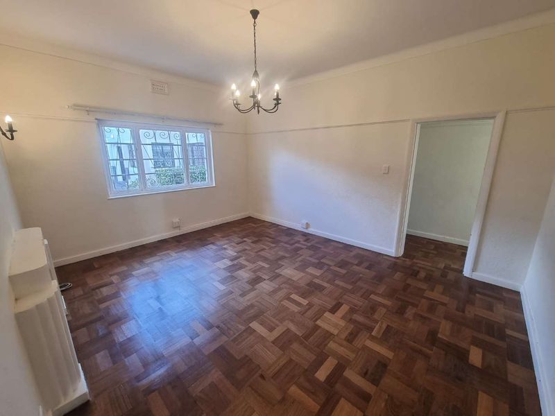 A bright and spacious living room featuring polished parquet flooring, a decorative chandelier, and a classic fireplace mantel.