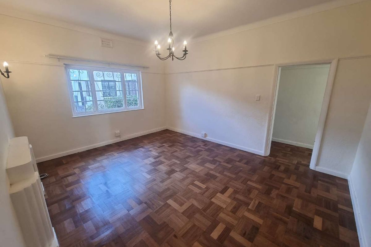 A bright and spacious living room featuring polished parquet flooring, a decorative chandelier, and a classic fireplace mantel.