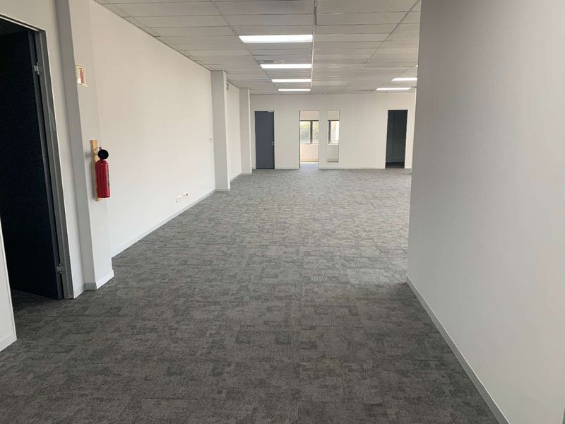 A spacious, open-plan office area featuring neutral carpet tiles, a suspended ceiling with recessed lighting, and multiple internal access points.