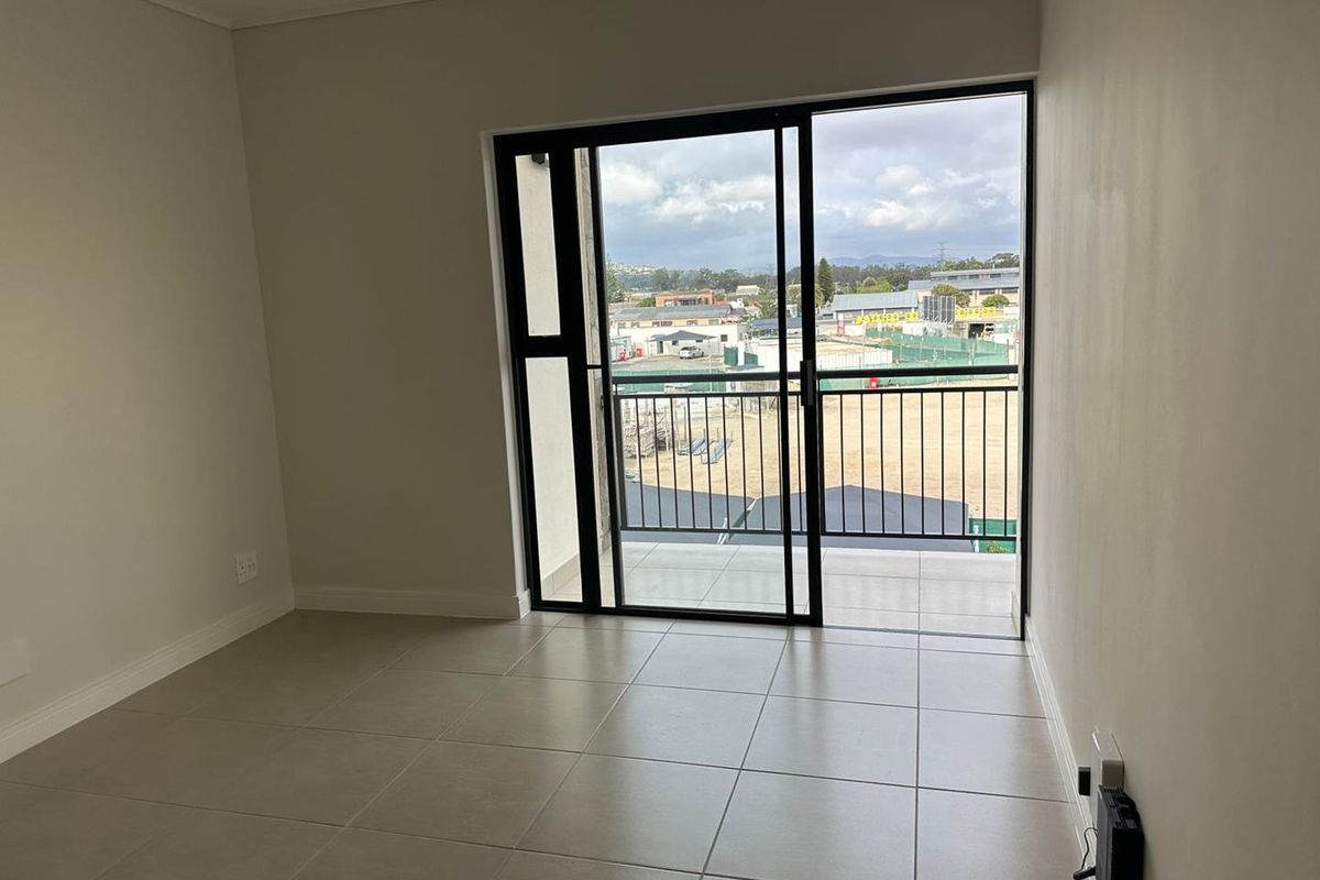 A bright, empty living area featuring neutral floor tiles and large sliding glass doors that open onto a private balcony with neighborhood views.