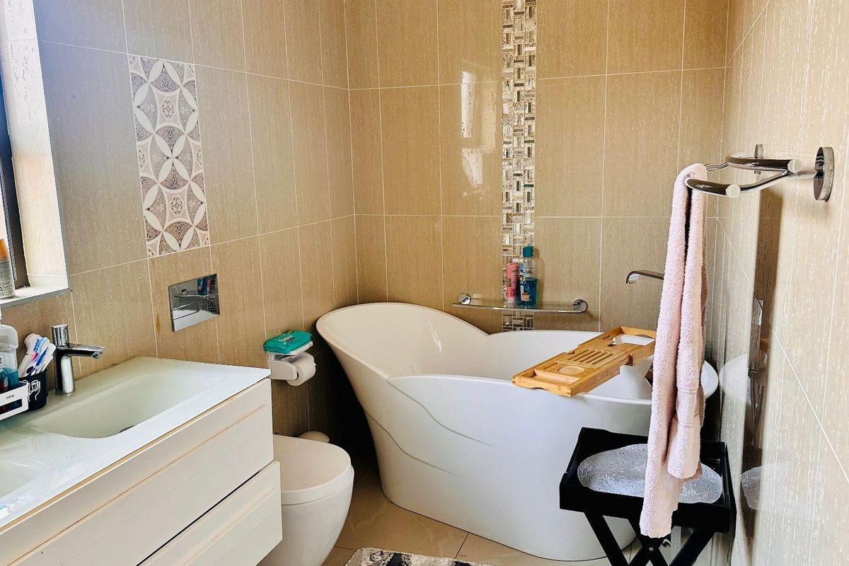 A modern bathroom featuring a freestanding bathtub, a wall-mounted vanity with a basin, and neutral wall tiling with decorative mosaic accents.