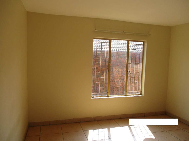 A vacant bedroom featuring tiled flooring and a window fitted with security bars, offering a neutral canvas for personalization.