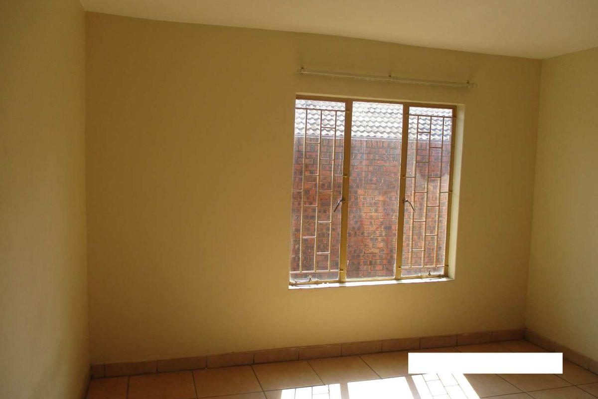 A vacant bedroom featuring tiled flooring and a window fitted with security bars, offering a neutral canvas for personalization.
