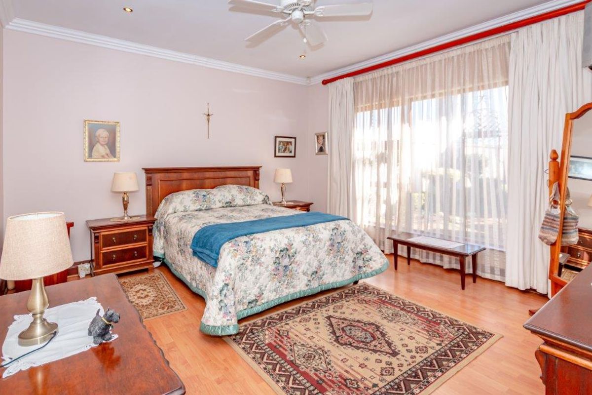 A well-maintained bedroom featuring laminate flooring, crown molding, and a ceiling fan, with large windows allowing for ample natural light.