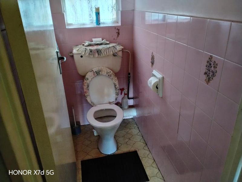 A compact bathroom featuring dated pink wall tiles and original vinyl flooring, offering significant potential for a modern renovation.