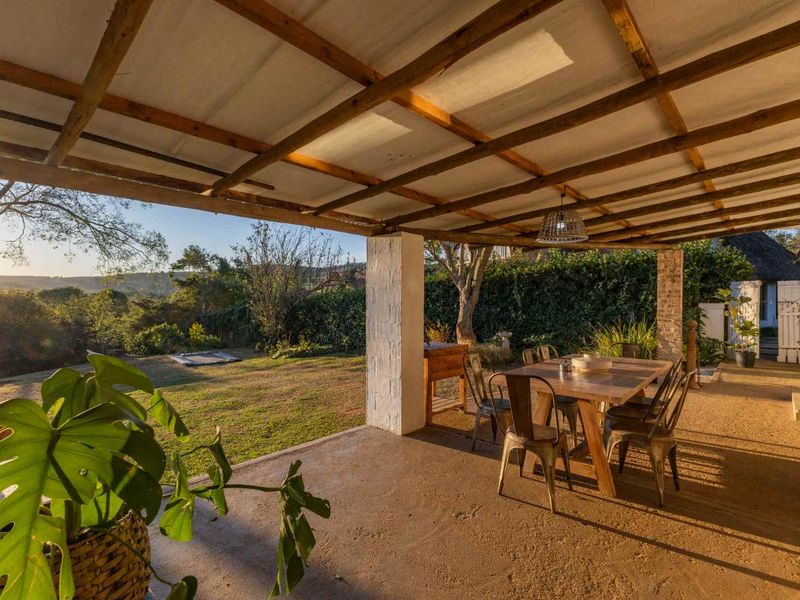 A spacious covered patio featuring a timber pergola roof and concrete flooring, offering scenic views of the surrounding garden and landscape.
