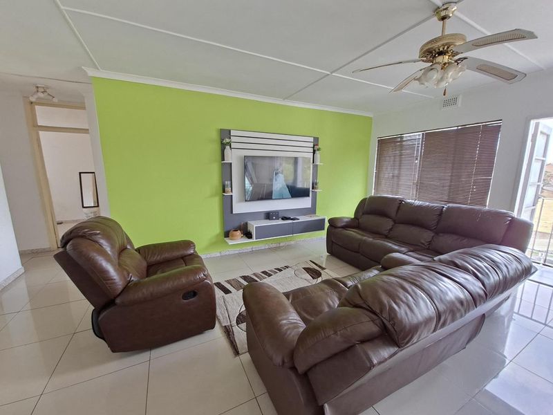 A living room featuring tiled flooring, a ceiling fan, venetian blinds, and a built-in media console unit.