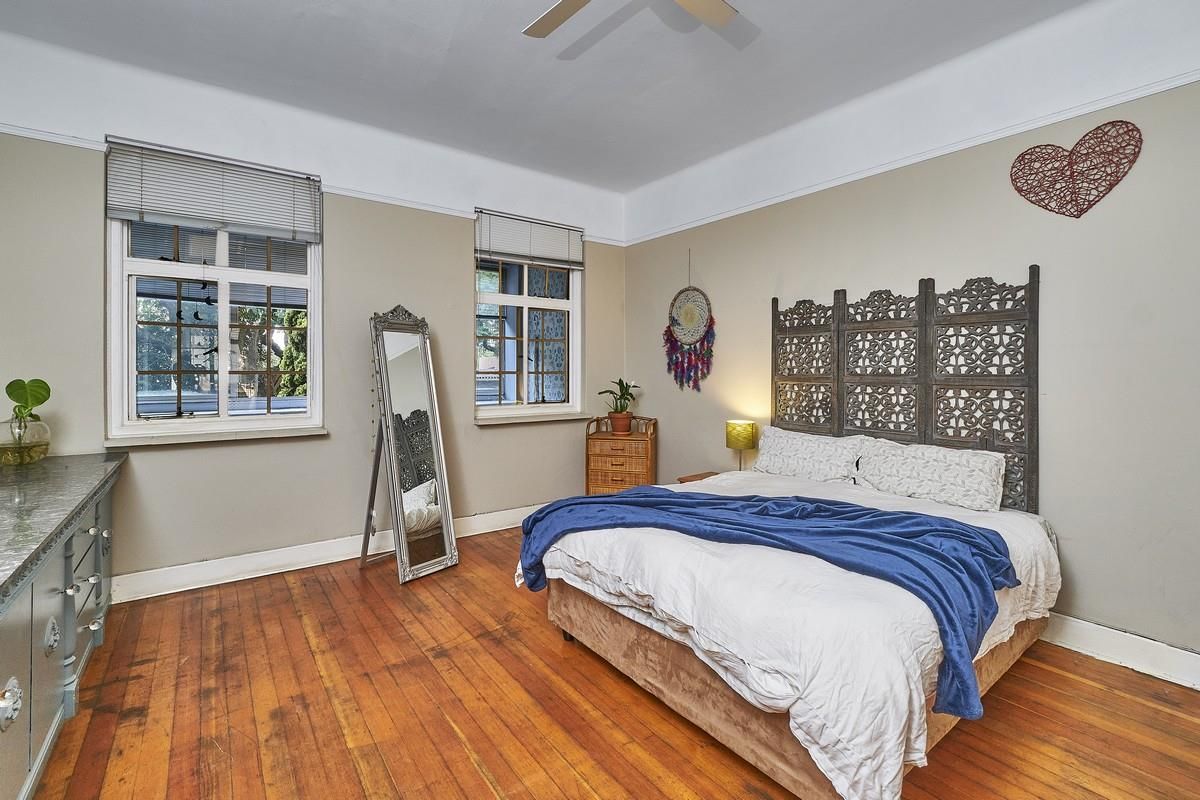A spacious bedroom featuring original timber flooring, high ceilings with crown molding, and two windows providing natural light.