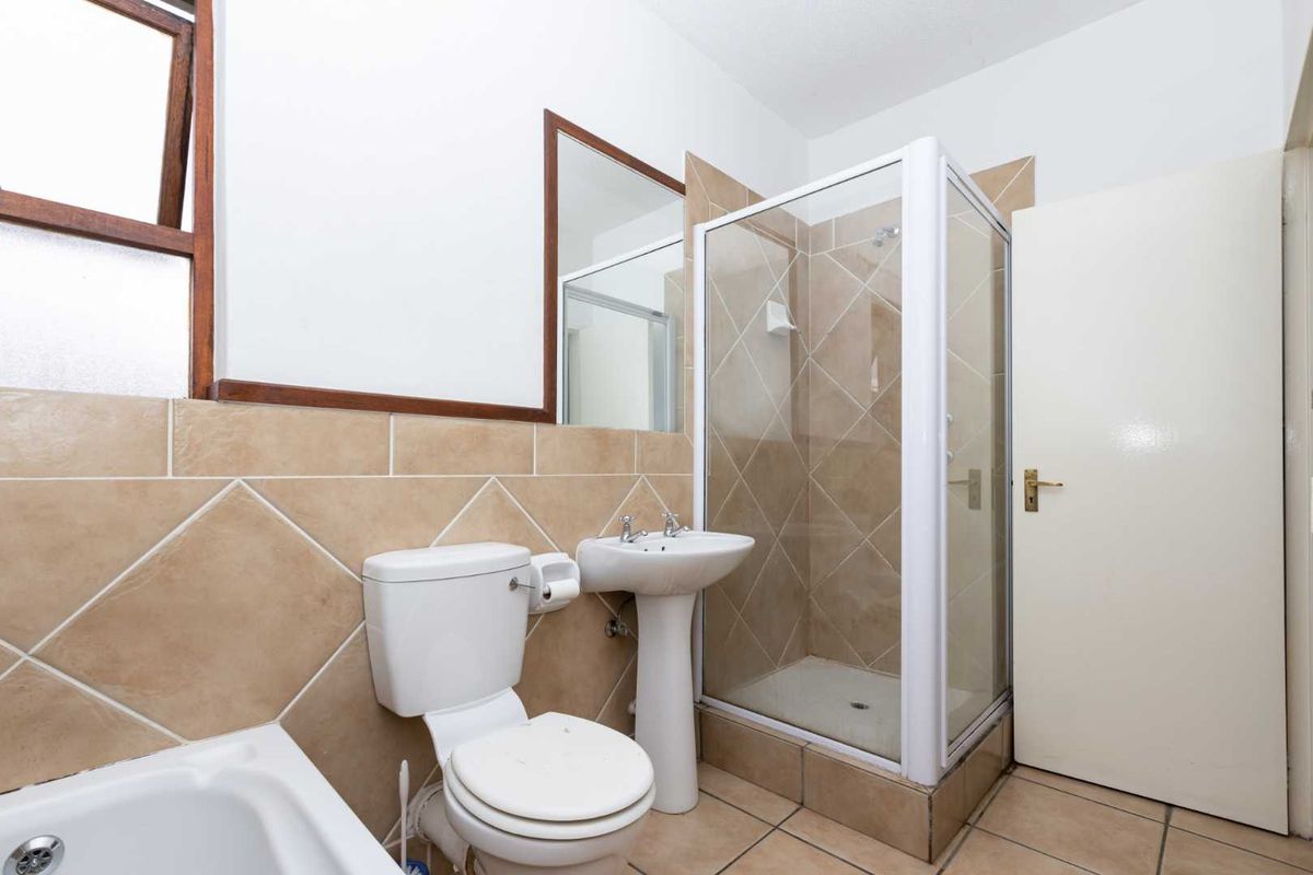 A functional bathroom featuring a shower enclosure, pedestal basin, toilet, and bathtub with neutral wall and floor tiling.