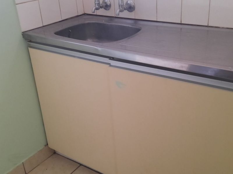 A functional laundry area featuring a stainless steel sink, dual taps, and built-in cabinetry with a tiled splashback.