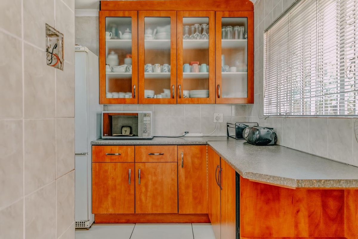 A functional kitchen area featuring wooden cabinetry, tiled walls, and a laminate countertop with integrated storage space.