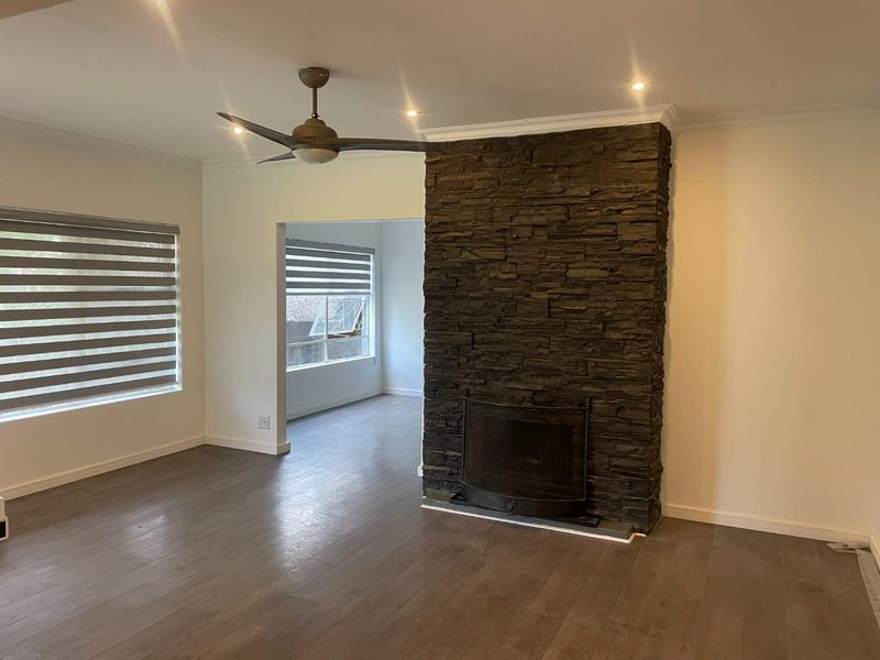 Spacious living room featuring a striking stone-clad fireplace, modern laminate flooring, recessed lighting, and a ceiling fan, offering a clean and neutral canvas.