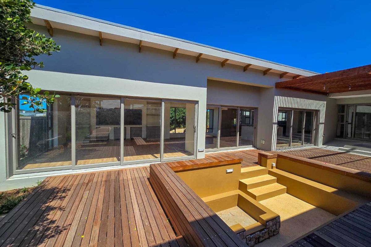 A spacious rear exterior featuring a large timber deck, a sunken seating area with built-in steps, and extensive sliding glass doors leading to the interior.
