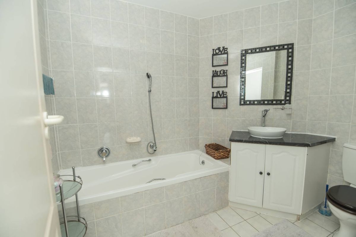 A functional bathroom featuring a built-in bathtub, a vanity with a vessel sink, and neutral wall tiling.