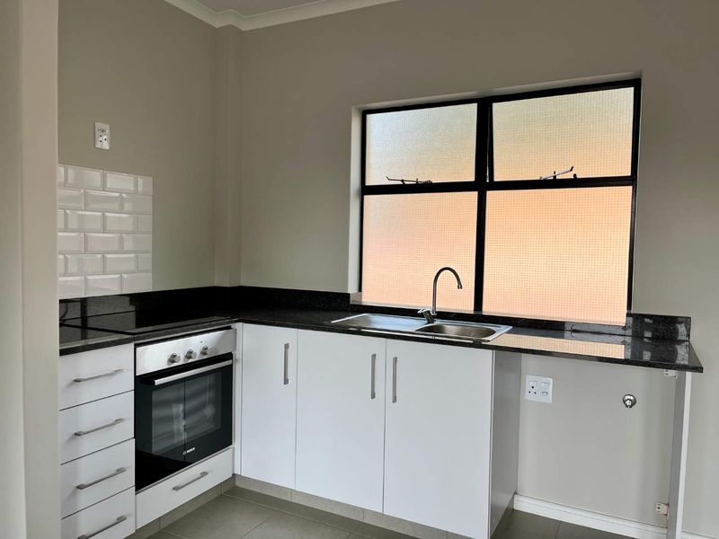 A clean, modern kitchen featuring white cabinetry, granite countertops, a built-in oven, hob, and a subway tile backsplash.