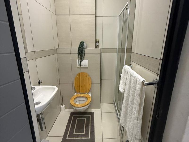 A modern, compact bathroom featuring floor-to-ceiling neutral tiling, a wall-mounted toilet, a pedestal sink, and a glass-enclosed shower.