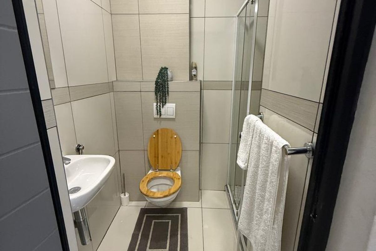A modern, compact bathroom featuring floor-to-ceiling neutral tiling, a wall-mounted toilet, a pedestal sink, and a glass-enclosed shower.