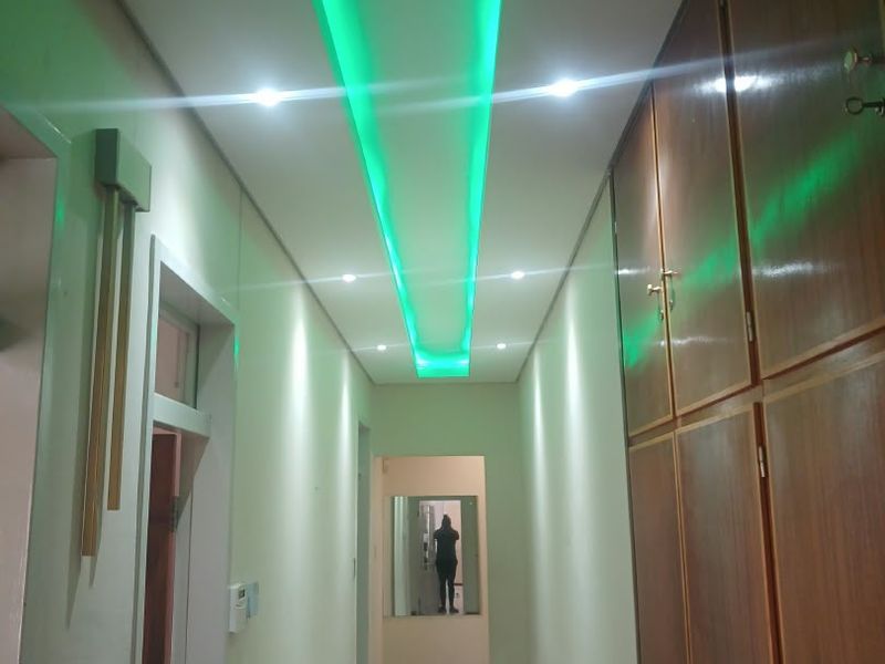 A well-lit hallway featuring built-in wooden storage cabinetry, tiled flooring, and modern recessed ceiling lighting with decorative green accent lighting.