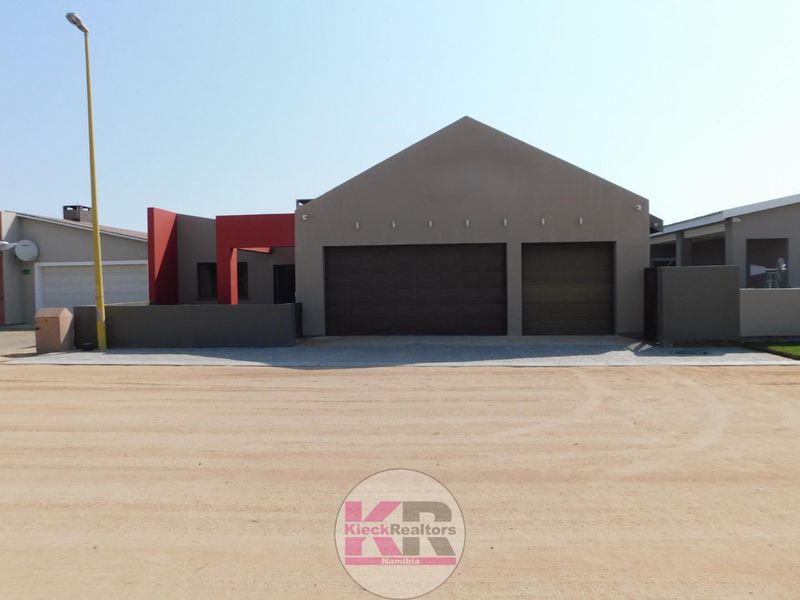 Front elevation of a modern house featuring a double garage, paved driveway, and contemporary architectural design with red accent walls.