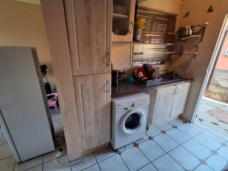 A functional kitchen area featuring laminate cabinetry, a built-in washing machine, stainless steel sink, and tiled flooring with direct access to an outdoor space.