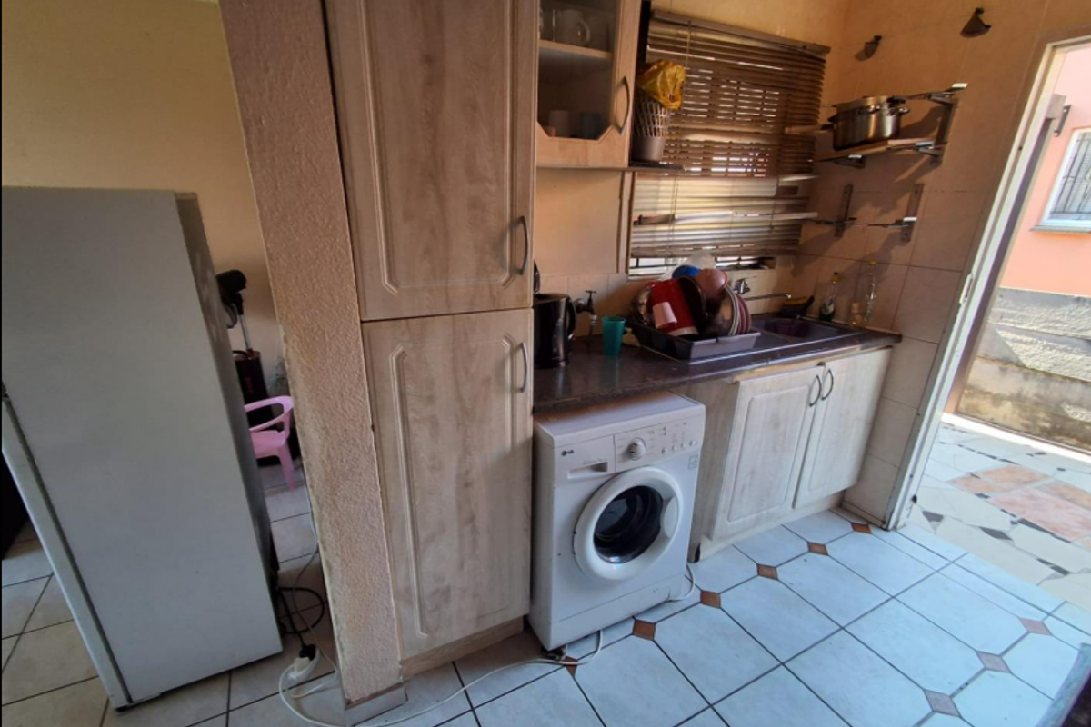 A functional kitchen area featuring laminate cabinetry, a built-in washing machine, stainless steel sink, and tiled flooring with direct access to an outdoor space.