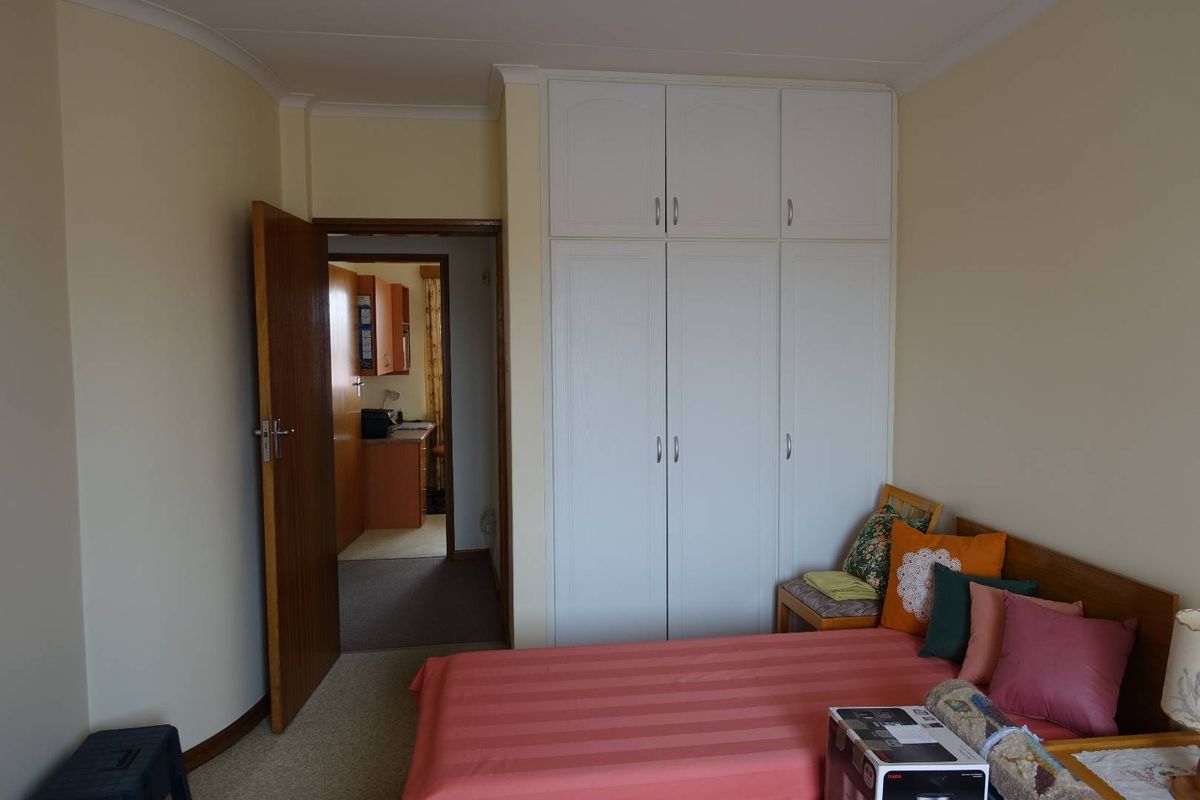 A bedroom featuring built-in white cupboards, coved ceilings, and a doorway leading to an adjacent room.