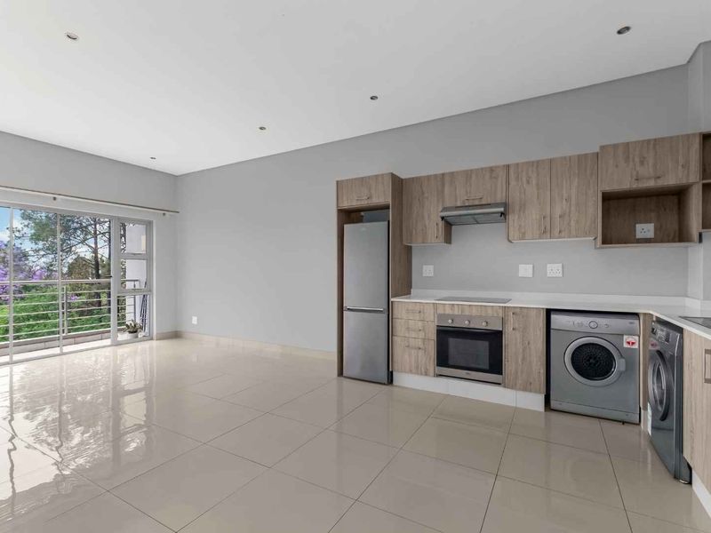Modern open-plan kitchen and living area featuring light wood cabinetry, integrated appliances, sleek tiled flooring, and a sliding door leading to a balcony.