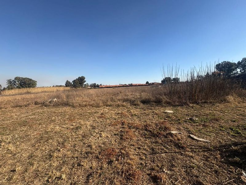 A wide-angle view of a vacant residential plot featuring natural dry grass and surrounding landscape.