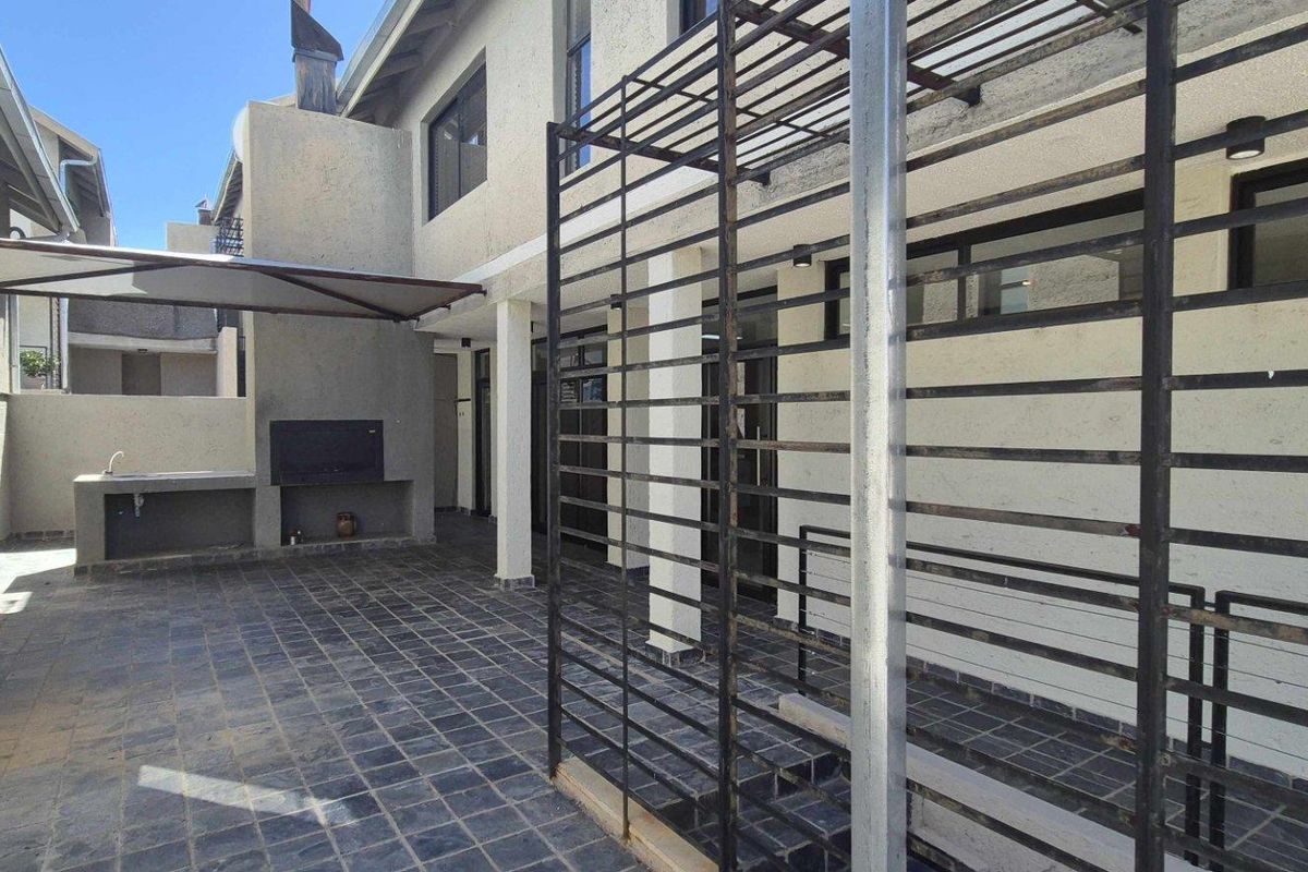 Rear patio area featuring a built-in braai, tiled flooring, and a metal security gate structure attached to the townhouse exterior.