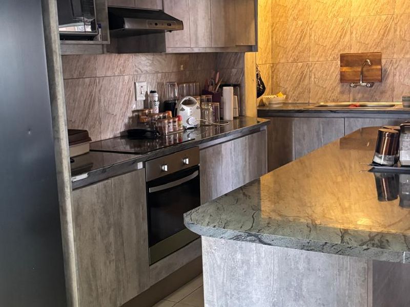 Modern kitchen featuring grey wood-grain cabinetry, stone countertops, integrated oven, extractor fan, and under-cabinet lighting with a functional breakfast island.